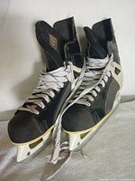 Pair of black CCM ice hockey skates with white laces showing front and top view, lightly used condition.