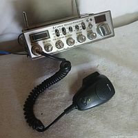 Front view of the Cobra Sound Tracker CB radio showing control panel, channel display, signal meter, knobs, and microphone attached via coiled cord.