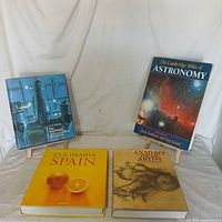 Four coffee table books displayed against a white backdrop: The National Air and Space Museum, Culinaria Spain, Anatomy for the Artist, The Cambridge Atlas of Astronomy