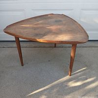 Front-side angle view of the triangular wooden Denmark table showing the tapered legs and surface patina.