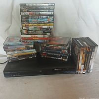 Overall view of Toshiba DVD player with 38 assorted DVDs stacked and arranged around it.