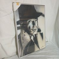 Framed black and white Humphry Bogart portrait print in silver metal frame with white protective corner covers.