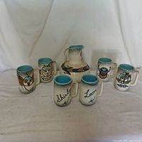 Photo showing one pitcher and six cups with Indigenous American style paintings.