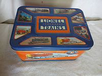 Metal Lionel storage container with colorful graphic prints of trains and Lionel logos on the lid and sides.