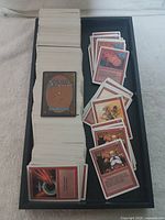 Black tray with approx 1000 Magic The Gathering game cards mostly stacked with some spread out showing card fronts, including red cards like Dwarven Warriors and Disintegrate.