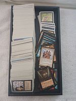 Large stack of Magic The Gathering cards in a box, some spread showing card faces and backs.