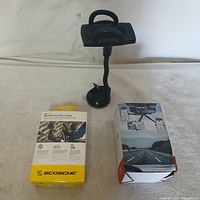 Photo of Scosche phone holder with flexible arm next to its original packaging box, displayed on a white surface.