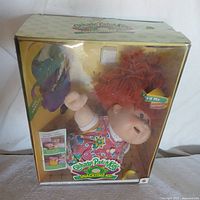 Front view of the doll in original yellow packaging with clear plastic window showing the doll with red yarn hair and dress.