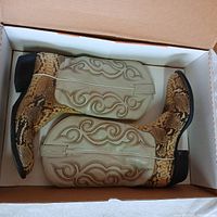 Pair of Toni Lama cowboy boots in original box showing snake skin foot and beige upper shaft with ornate stitching, black heels and toes.