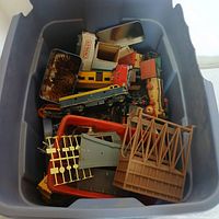 Top view of tub filled with assorted train parts including a plastic bridge structure, train cars, and signal light base.