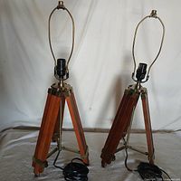Pair of vintage wooden tripod lamps with brass fixtures standing against a white background, showing full height and structure.