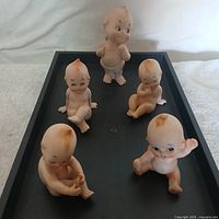 Photo showing all five Lefton Baby Kewpie porcelain figurines on a black display tray, each with distinct poses and detailed painted features.