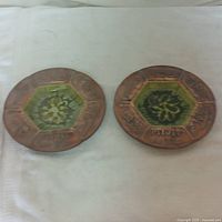 Top view of two round copper-tone Walt Disney ashtrays, each with hexagonal green center featuring a floral design.