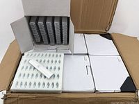 Open box showing multiple white cardboard boxes containing white plastic casings, with one casing displayed separately on top.