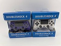 Two Doubleshock 4 wireless controllers in original packaging, one transparent purple and one white.