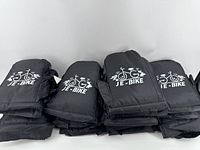 Multiple pairs of black nylon hand covers with white JE-Bike logo, folded and stacked