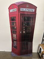 Front and side view of large cardboard Doctor Who phone booth cutout showing red color, windows, 'TELEPHONE' signage, and door handle details.