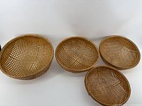 Four round woven baskets arranged side by side showing similar shallow depth and uniform height.