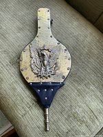 Front face of the bellows showing the brass panel with eagle emblem in relief and nozzle at bottom.