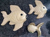 Three ceramic fish wall decorations laid on a black surface, showing size variations and details.