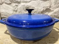 Side view of the blue Dutch oven with lid, showing the height and shape, with two side handles and black knob.