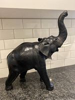 Black leather wrapped elephant figurine on counter with tile background, showing full side profile.