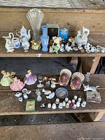 Wide view of two wooden shelves displaying an assortment of miniature collectibles including porcelain dolls, tea sets, thimbles, and souvenir items.