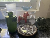 Front view of the lot showing all items on a dark surface by a window, including glassware, figurines, and decorative plate.