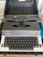 Front view of Olympia manual typewriter showing keyboard layout, platen, and paper feeder.