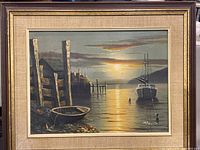 Framed vintage painting of a sunset maritime scene with a dock, rowboat, and sailboat, signed at bottom right corner.