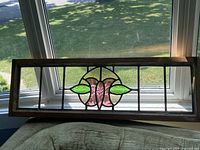 Front view of stained glass panel showing floral design with pink, green, and clear textured glass in a wood frame.