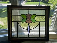 Full view of stained glass window panel with floral design framed in wood.