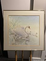 Framed artwork of adult swan and cygnets in water with reeds, soft pastel colors, signed by Glen Loates.