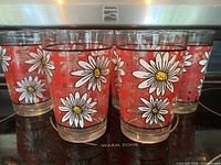 Photo showing side view of 4 vintage glasses with white daisy flower designs on an orange checkered background