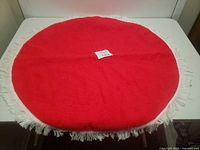 Full view of circular red Christmas tree skirt with white fringe on edges laid flat.