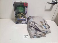 Photo showing Hulk action figure in box beside folded Transformers double sheet, on white surface.