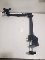 Black adjustable monitor arm with clamp for desk mounting, laying flat on a white surface