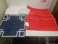 White queen sheet with four red pillow covers and one blue pillow cover arranged on a table showing colors and patterns clearly.