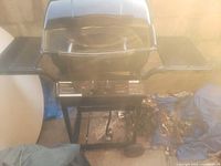 Front view of black gas barbecue grill with lid and two side shelves, control knobs on front panel.