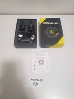 Two LED car light bulbs in foam insert, with power cables and connectors, placed alongside the Carrover branded box and instruction leaflet on a white surface.