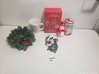 Photo showing all Christmas items including mug, wreath, ornament kit, snowman ornament, Santa hanging decoration, and tin.