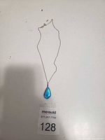 Photo of women's necklace with blue tear drop pendant laid flat on a white surface showing the full chain and pendant.