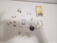 Photo of various costume earrings arranged on white surface with lot tag number 62