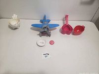 White ceramic measuring cups, toy airplane, small dishes, and red button pin arranged on a white surface