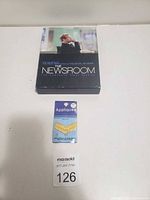 Photo of The Newsroom DVD box set and a gold chevron applique patch on a flat surface with a MaxSold lot number card.