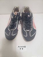 Front and top view of the black Puma shoes with white and pink accents, showing the laces and toe design.