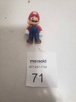 Plastic Super Mario figurine toy with red hat, blue overalls, white gloves, brown shoes