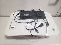 White HP all-in-one printer scanner copier with control panel, display, power cord, and USB cable on top.