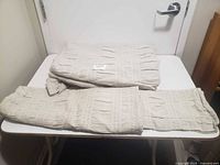 Two beige queen bed sheets folded on a white surface, showing texture and stripe pattern.