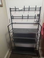 Black metal over-the-door shoe rack with shelves and hanging hook racks mounted on a white door.